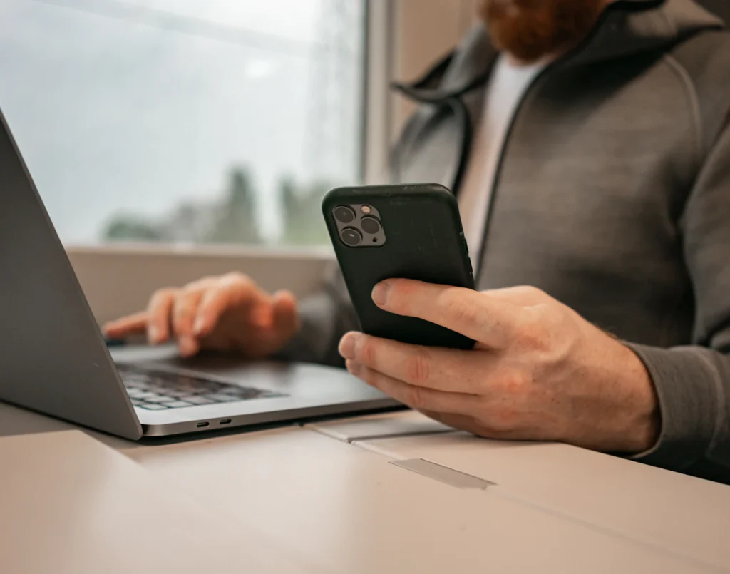 Man checking new emails on his phone while working on a laptop